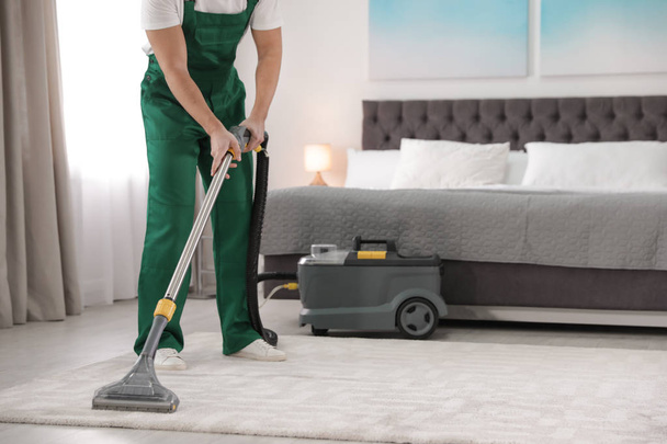 Professional janitor removing dirt from carpet with vacuum cleaner in bedroom, closeup. Space for text - Фото, изображение