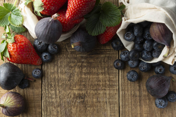 Frame met vruchten met aardbeien, bosbessen, vijgen op rustieke gestructureerde achtergrond. De achtergrond van de fruit voor het ontbijt met kopie ruimte. Plat lag, top uitzicht. - Foto, afbeelding