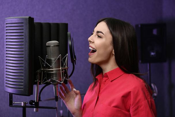 Νεαρή τραγουδίστρια με μικρόφωνο καταγράφει το τραγούδι στο studio - Φωτογραφία, εικόνα