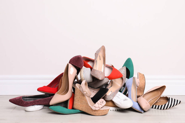 Heap of different shoes on floor against light wall - Foto, immagini