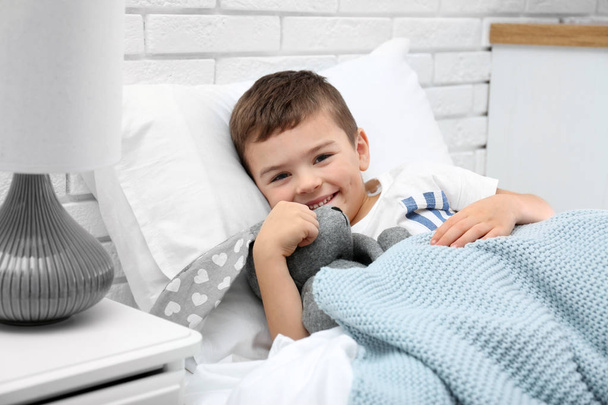 Lindo niño con conejito de peluche descansando en la cama en el hospital
 - Foto, Imagen