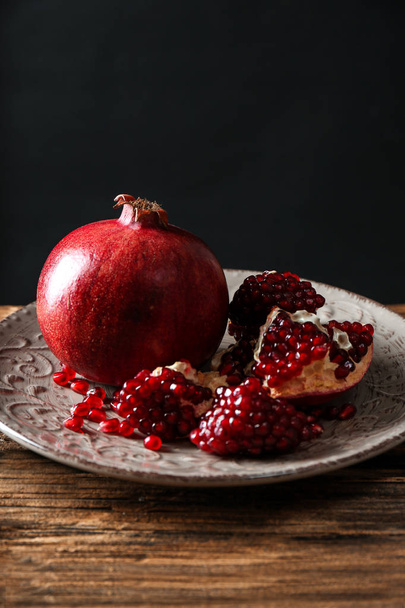 Plate with ripe pomegranates on table against black background - Photo, Image