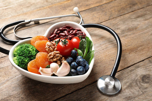 Bowl with heart-healthy diet products and stethoscope on wooden table. Space for text - Foto, Bild