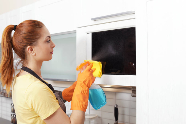 Woman cleaning microwave oven with rag and detergent in kitchen - Photo, Image