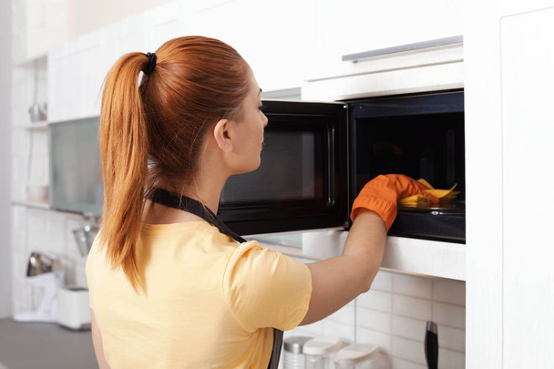 Woman cleaning microwave oven with rag in kitchen - Foto, Imagem