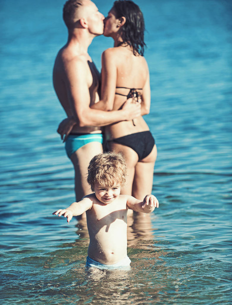 Child with kissing father and mother. Family travel with kid on mothers or fathers day. Summer vacation of happy family. Love and trust as family values. Mother and father with son in sea on beach. - Photo, Image