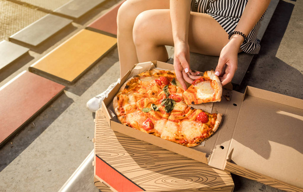 Jovem feliz segurando pizza quente na caixa, assento ao ar livre no parque
 - Foto, Imagem
