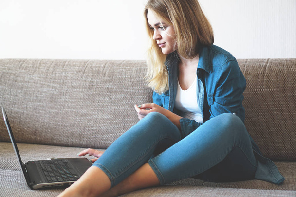 Smiling blonde relaxing on couch with her laptop at home in the living room - Photo, image