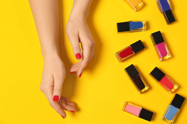 Woman with red manicure and nail polish bottles on color background, top view - 写真・画像