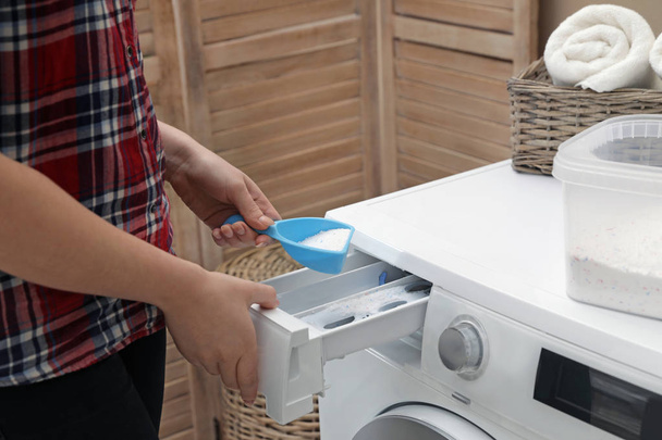 Woman pouring detergent powder into washing machine in laundry room, closeup - Фото, зображення