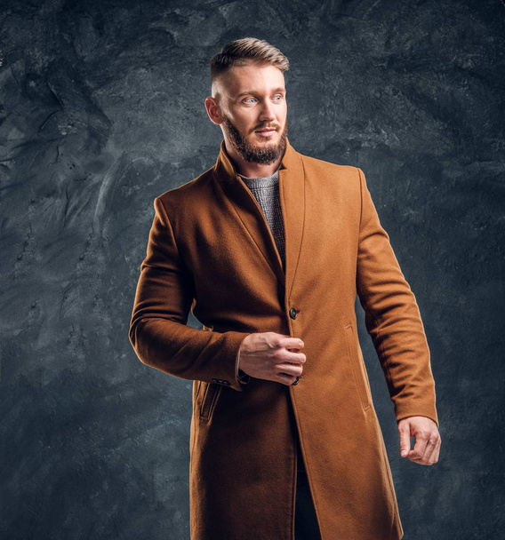 Портрет стильного мужчины в полусезонном пальто. Мужская красота, сезонная мода. Студийное фото на фоне темной стены
 - Фото, изображение