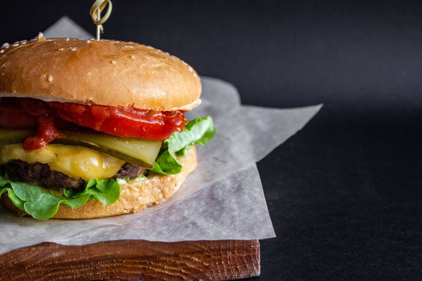 friss ízletes sajt Burger hasábburgonyával és zöldségekkel, fekete alapon - Fotó, kép