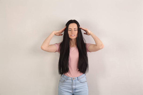 Attractive young brunette woman with long hair is standing by the grey background having strong headache and holding hands by the head. Wearing jeans and pink shirt - 写真・画像