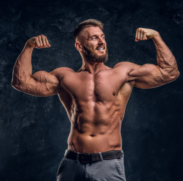 Modelo masculino con el cuerpo muscular posando para una cámara. Foto del estudio contra un fondo de pared oscuro
 - Foto, imagen