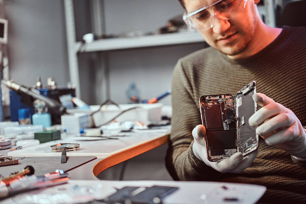 Technicien électronique montrant un smartphone avec un corps cassé dans un atelier de réparation
 - Photo, image