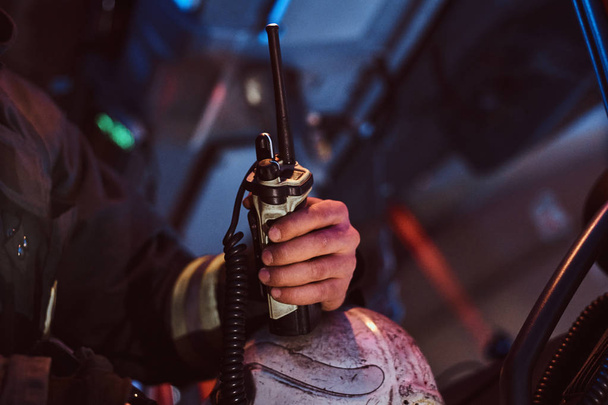 Fireman in a protective uniform sitting in the fire truck and holding walkie-talkie. Hand close up. - Photo, Image