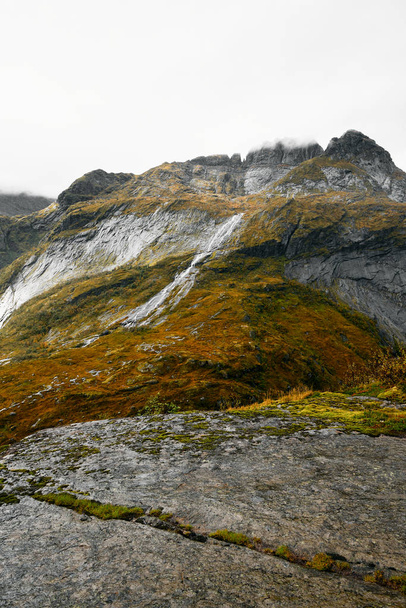 Uitzicht vanaf de rand van een klif in de bergen van de eilanden van de Lofoten in Noorwegen in een vallei met een waterval en meer. De plek ligt in Noord-Noorwegen in de buurt van Solvagen in de bergen. Het is een lichte, regenachtige en koude dag in September. Waterval             - Foto, afbeelding