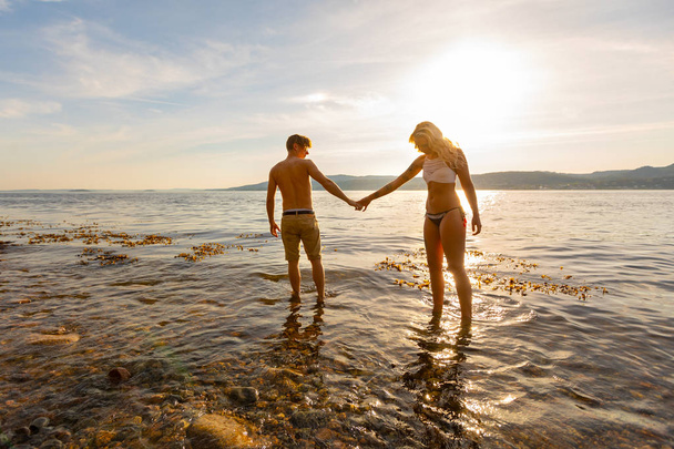 Beautiful couple holding hands and walks at the sea shore in the evening - Photo, Image