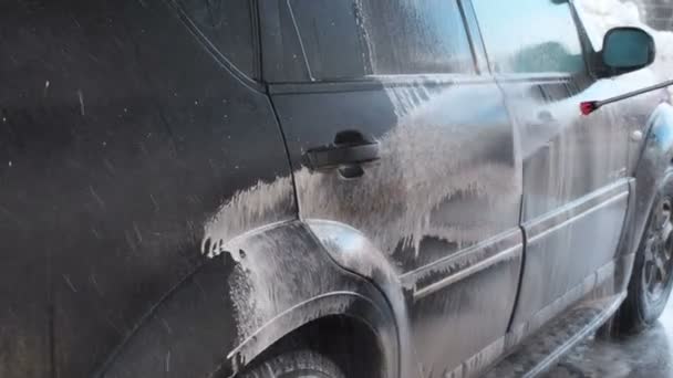 Video en cámara lenta de un proceso de lavado de autos en un auto-servicio de lavado de autos. Un chorro de agua con un lavado de alta presión de la suciedad del auto. Vista lateral. Detergente espumado drena de la superficie de la
 - Metraje, vídeo