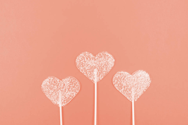 Lollipops in the shape of hearts on a coral background. Top view. Flat lay with copy space. - Fotografie, Obrázek