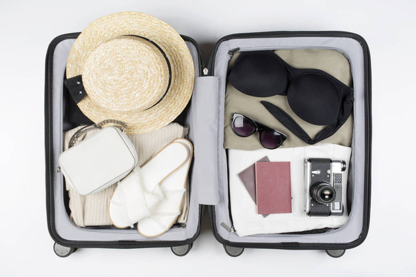Open suitcase packed for travelling. Hat, glasses, sandals, swimsuit, bag, passport - Foto, imagen
