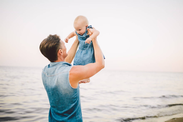 Téma šťastné otcovství. Osamělý otec Kavkazský mladík držící dítě dcera dítě začíná chodit jeden rok v létě na písečné pláži s výhledem na moře obzor - Fotografie, Obrázek