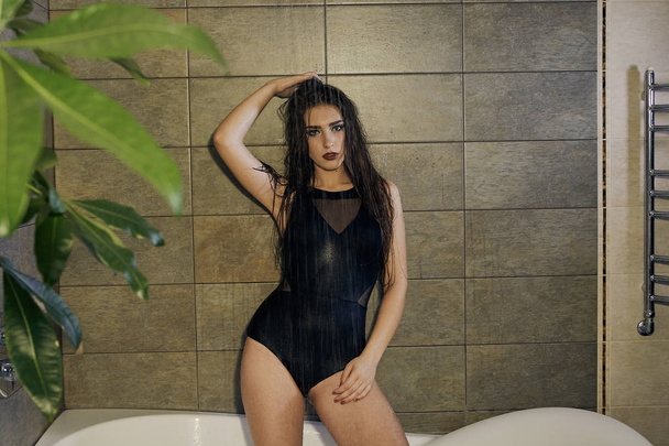 Chica en un traje de baño negro tomando una ducha para el diseño de concepto
. - Foto, imagen