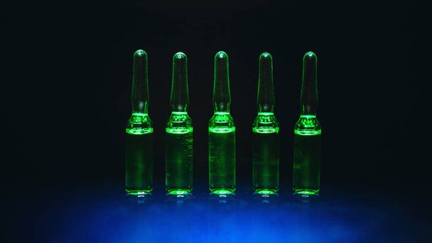 medical preparations. for the treatment of diseases. ampoules with green liquid on a black background. artistic dark filter. low key photo - Фото, зображення