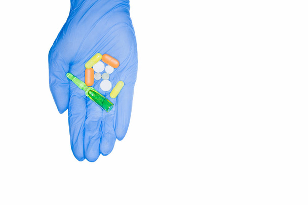 Растрата больничных наркотиков. Зеленые капсулы, таблетки, ампулы держатся вручную в медицинской перчатке, изолированы на белом фоне
. - Фото, изображение