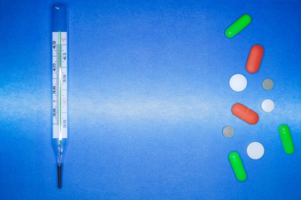Медицинский термометр и цветные таблетки на голубом фоне. здравоохранение и концепция оказания первой помощи
. - Фото, изображение