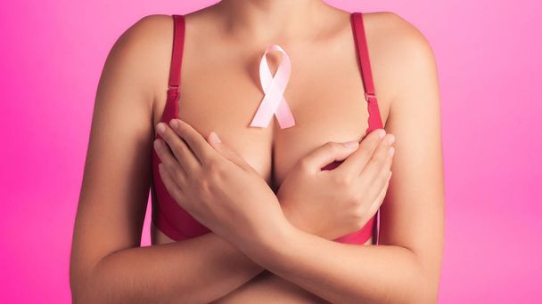health, medicine, beauty concept - naked woman rad bra with Pink Breast Cancer awareness Ribbon. Support of patients with oncology. close-up background - Fotografie, Obrázek