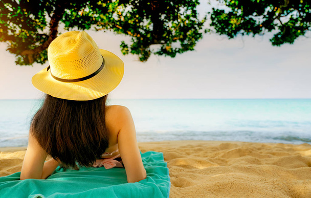 Задний вид счастливой молодой азиатской женщины в розовом купальнике и соломенной шляпе расслабиться и насладиться отдыхом на тропическом песчаном пляже под елкой. Девушка в моде летних каникул. Сексуальная модель красоты. Летние вибрации
. - Фото, изображение