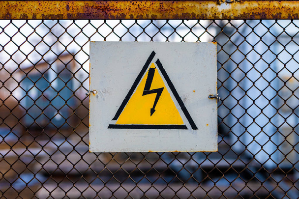 Merkki varoitus vaaroista korkea sähköjännite roikkuu verkkoaidan, joka ympäröi voimalinjan sähköasema
. - Valokuva, kuva