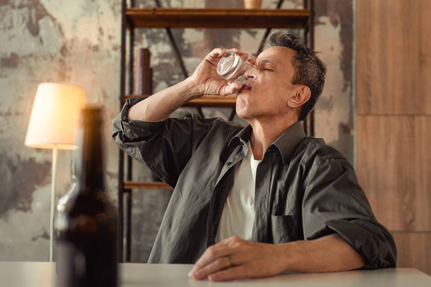 Shabby adult man emptying glass of alcohol with one sip - Zdjęcie, obraz