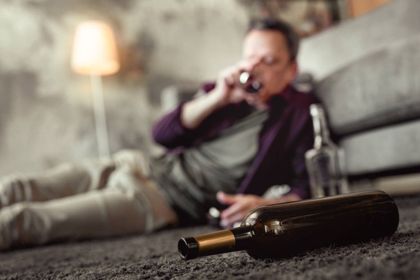 Adult man lying on carpet in living room with empty bottles around - Фото, зображення