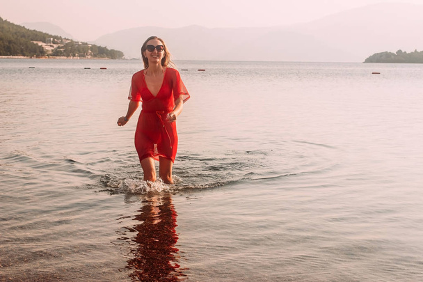 smiling woman in red beach tunic running across the sea - Fotografie, Obrázek