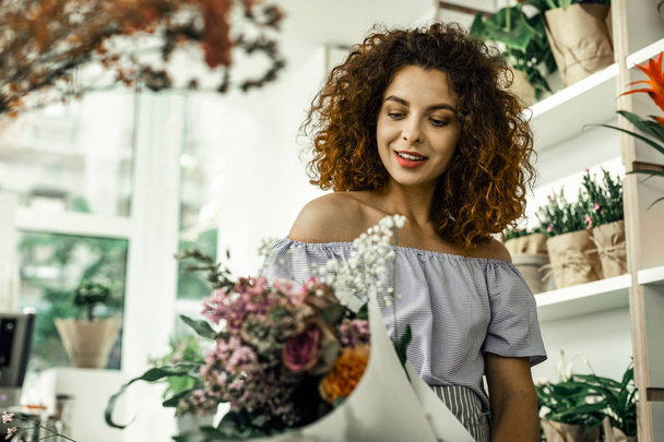 Curly florist feeling satisfied while looking at nice perfect bouquet - Fotografie, Obrázek