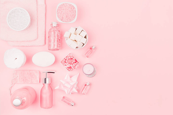 Cosmetic products and accessories in pink color - cream, bath salt, essential oil, soap, towel, sponge, pearls, bottles, bowl on pink background, top view. - Photo, Image