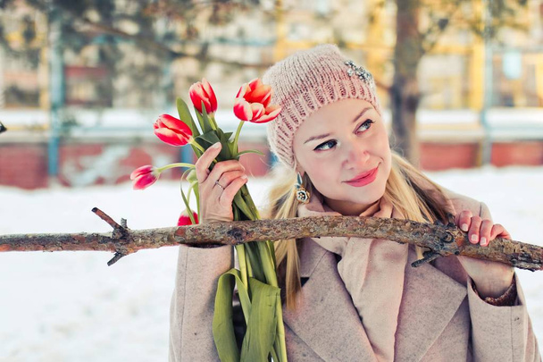 mooie blonde vrouw in winter kleding met rode tulpen. Portret van een gelukkige vrouw. - Foto, afbeelding