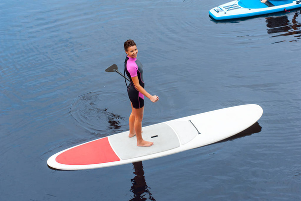 Joyful woman paddling on stand up board on blue river - Фото, зображення