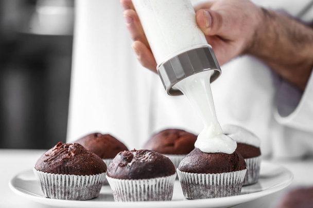Male confectioner cooking tasty cupcakes in kitchen, closeup - Photo, image