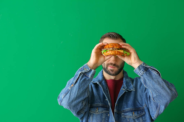 Man eating tasty burger on color background - Foto, afbeelding