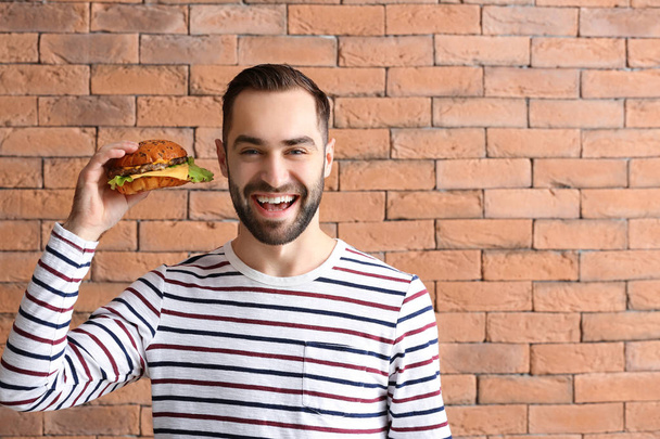 Man with tasty burger against brick wall - Foto, Imagem