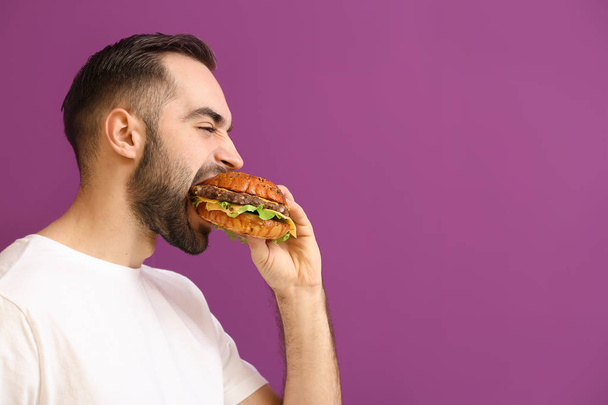Ember eszik ízletes burger, színes háttérrel - Fotó, kép