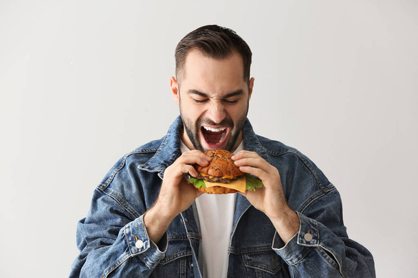 Man eating tasty burger on light background - Foto, Imagen