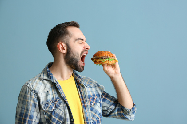 Man renk arka plan üzerinde lezzetli hamburger yemek - Fotoğraf, Görsel