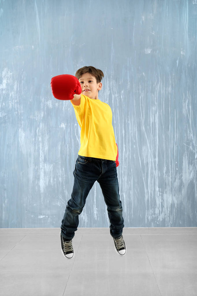 Cute little boy in boxing gloves jumping against grey wall - Фото, зображення