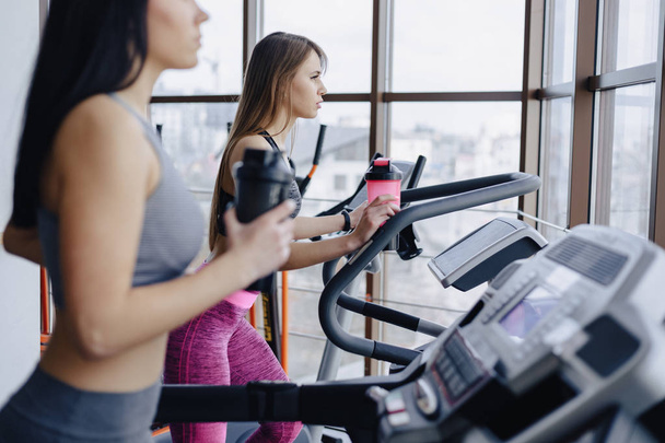 Girls in the gym are trained on treadmills and drink water, smiling - Φωτογραφία, εικόνα