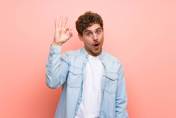Blonde man over pink wall surprised and showing ok sign - Photo, Image