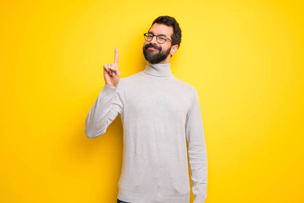 Homem com barba e gola alta mostrando e levantando um dedo em sinal do melhor
 - Foto, Imagem